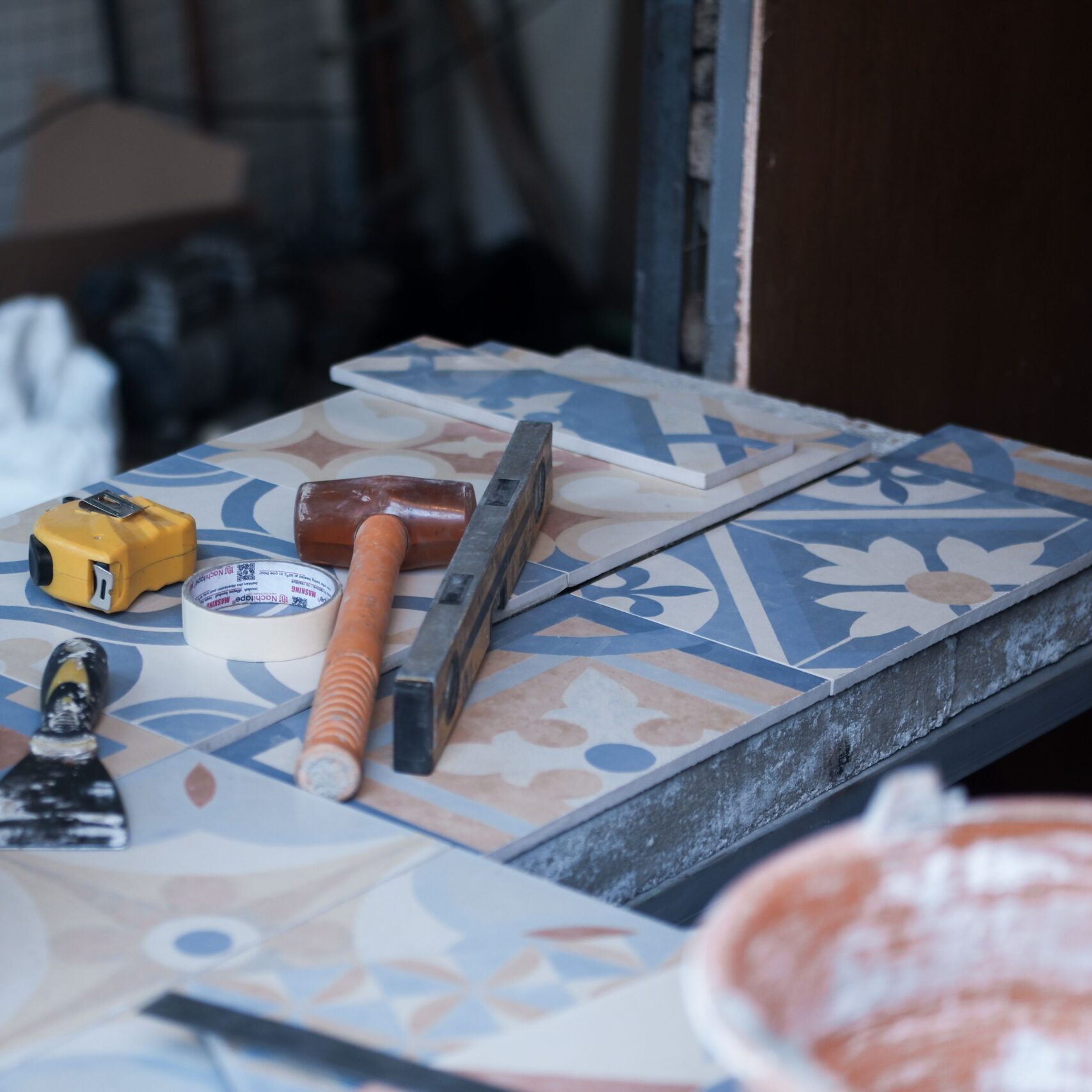 Tools and tiles on a construction site, ready for tiling work. Includes trowel, tape measure, and adhesive tape.