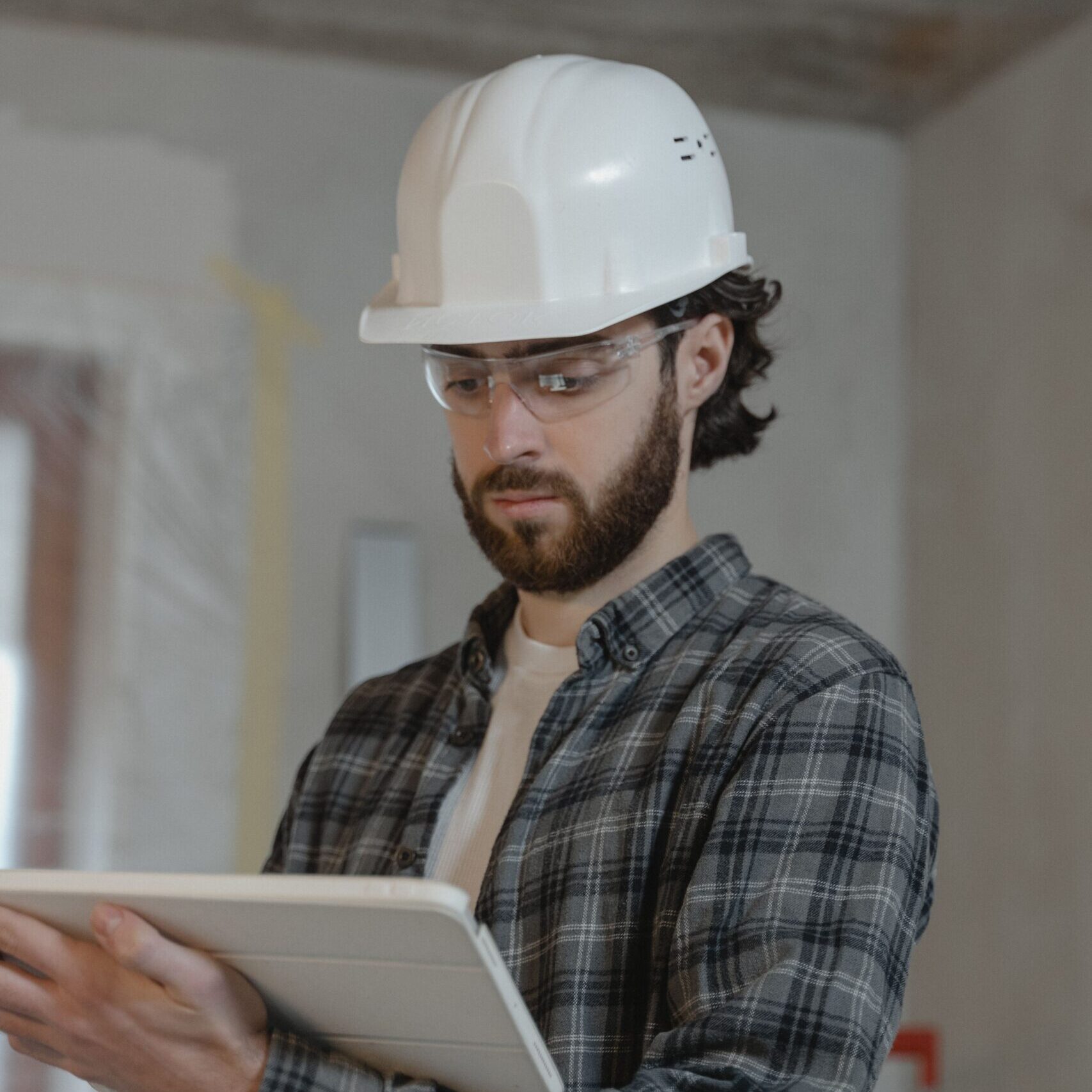 Male construction engineer assessing building plans indoors, wearing a hard hat.